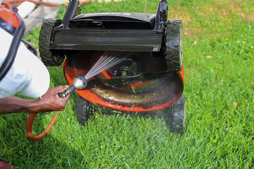 Cleaning and spraying underside of mower with garden hose
