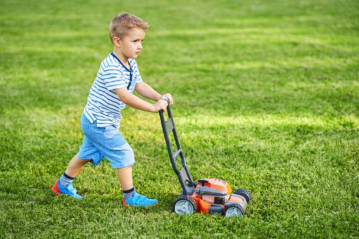 Toddler boy pretending to mow the lawn with toy mower